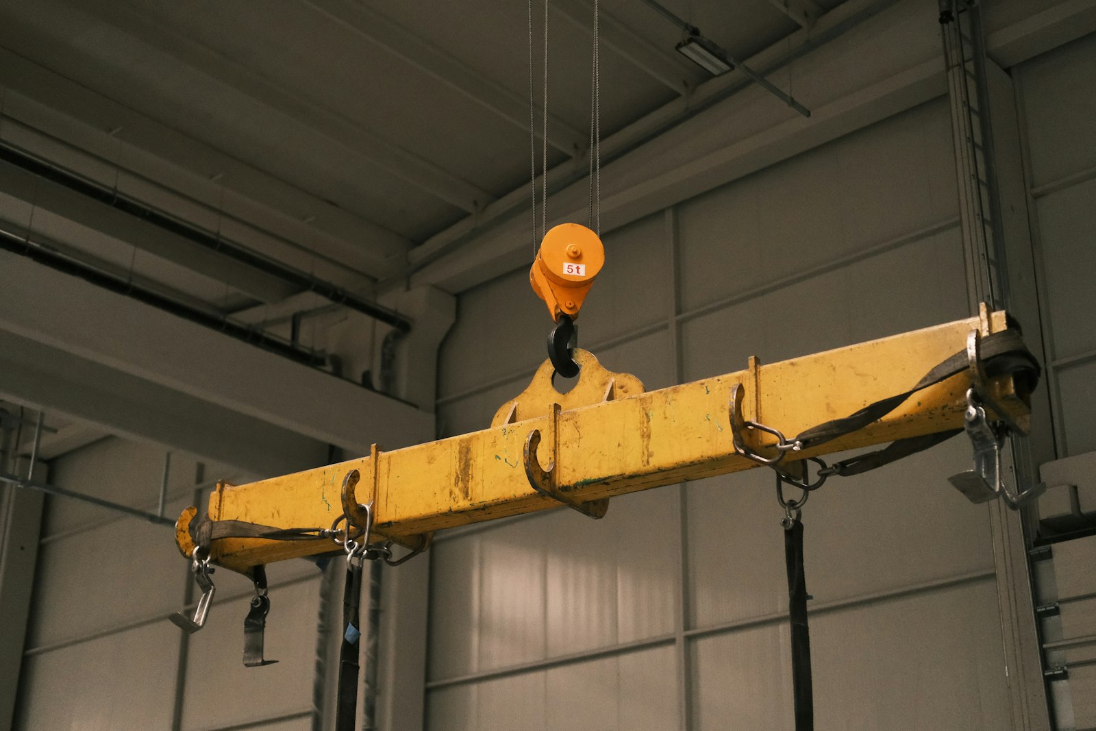 Yellow spreader beam on a crane hook with webbing slings and shackles